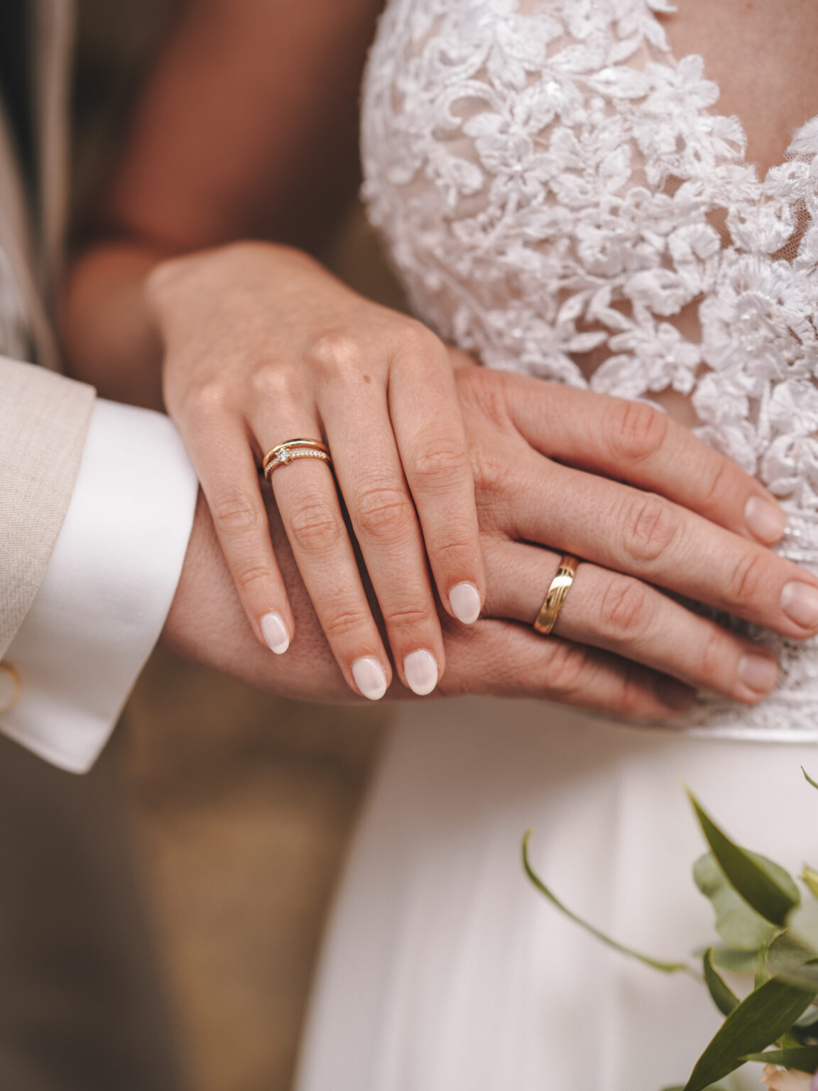 Nahaufnahme der Hände eines Paares mit Eheringen, die Braut in einem Spitzenkleid – ideal, um Erinnerungen an Ihrer gewählten Hochzeitslocation oder einer intimen Privatfeier festzuhalten.