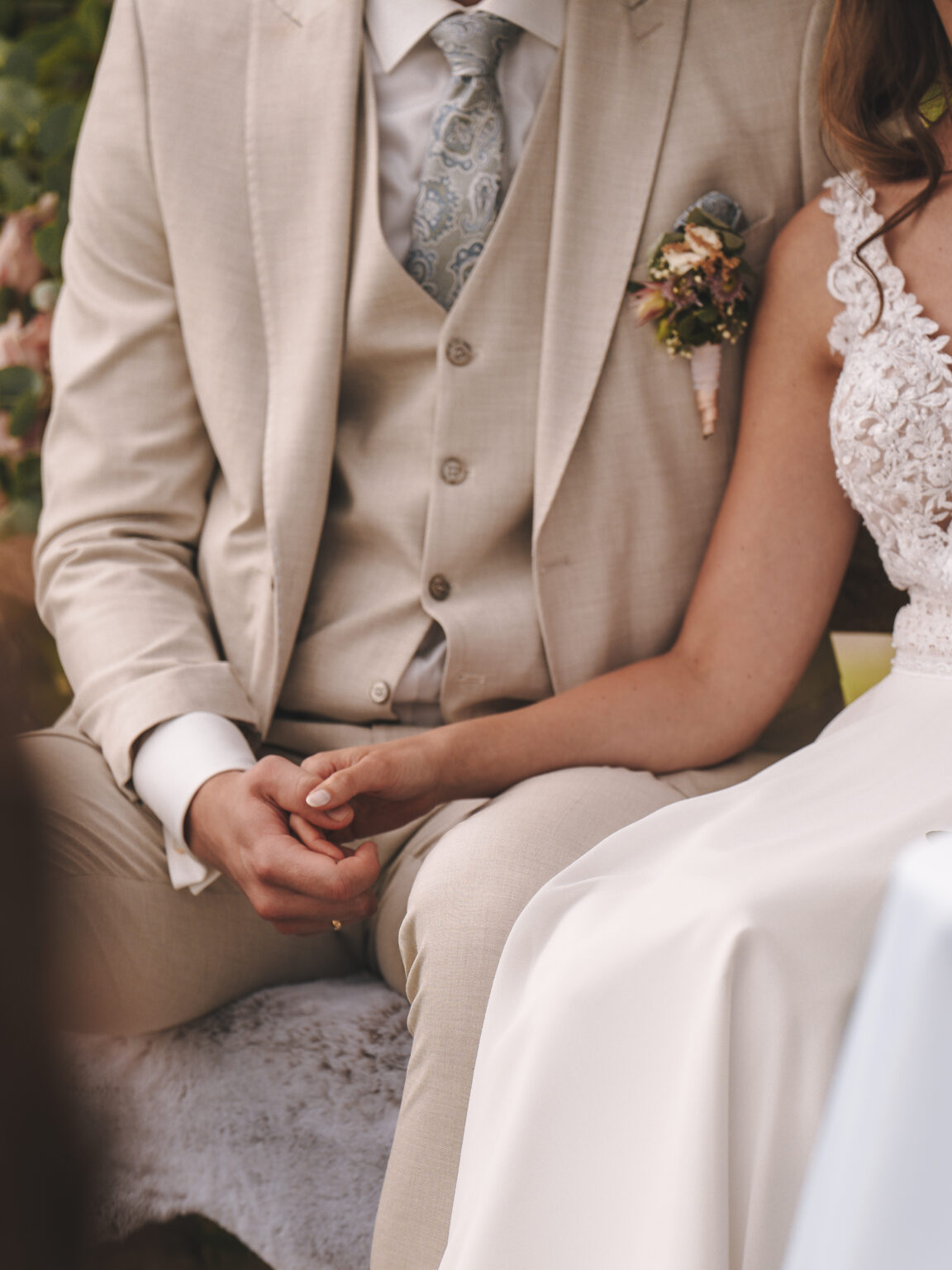 Ein Brautpaar sitzt eng beieinander, hält Händchen und trägt elegante Hochzeitskleidung – diese Kulisse im Freien macht diesen Veranstaltungsort zum perfekten Ort für jede private Feier oder einen besonderen Anlass.